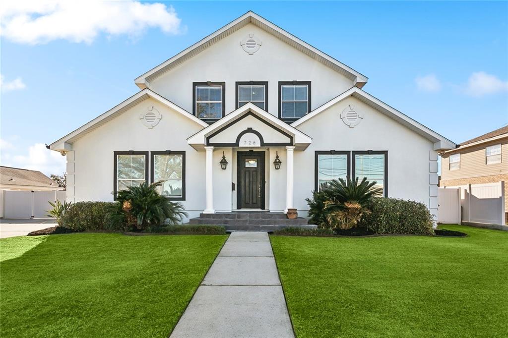 White two-story house with black-trimmed windows, covered entry, and a green front lawn.