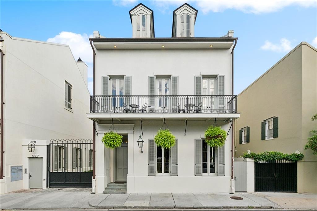 White New Orleans home with a wrought-iron balcony, shuttered windows, and hanging plants.