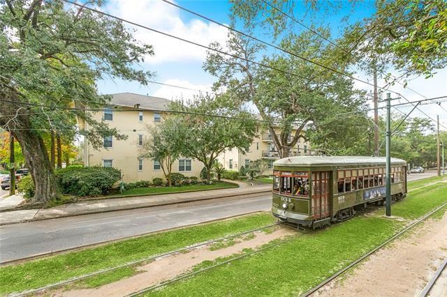 Apartment building beside a vintage streetcar on a tree-lined street.