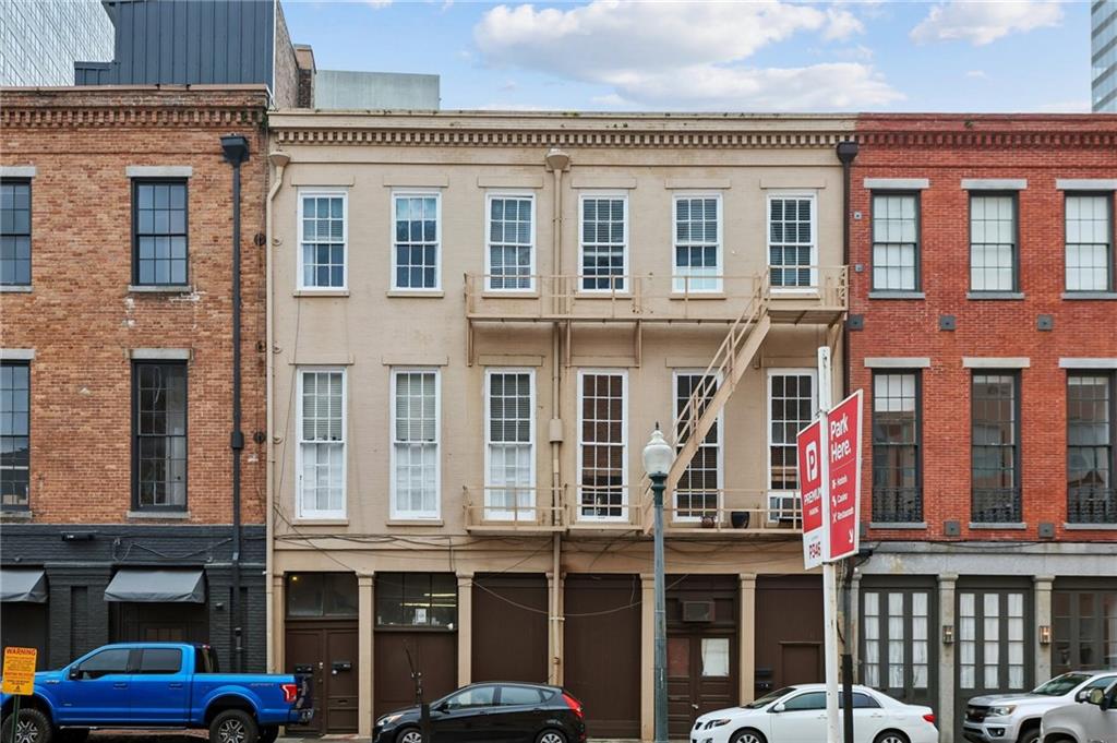 Beige multi-story building with a wooden balcony and exterior staircase between brick buildings.