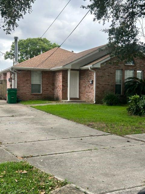 Single-story brick house with a tan roof, white entry, front lawn, and concrete driveway.
