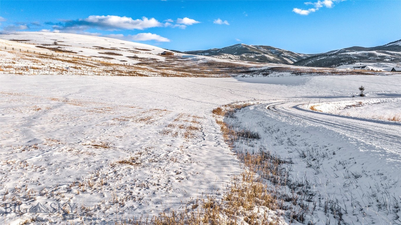 Snow-covered vacant lot with a curving road and mountain views.