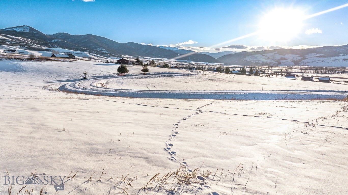 Snow-covered vacant lot with mountain views, a curved road, and footprints.