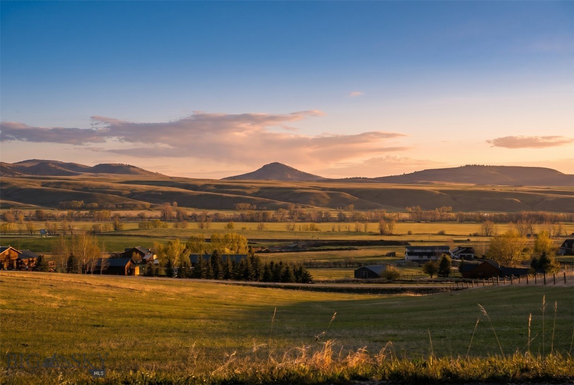 Open fields and scattered homes beneath rolling hills at sunset.