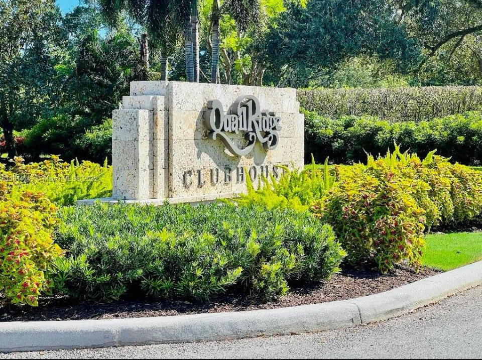 Quail Ridge Clubhouse entrance sign amid tropical landscaping.