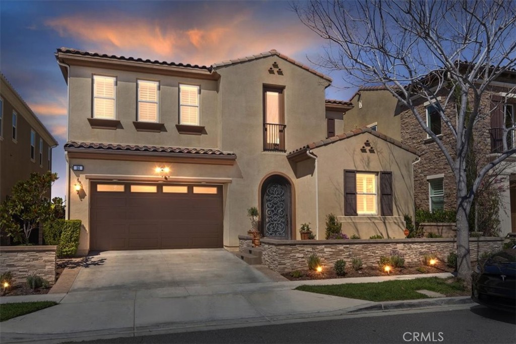 Two-story stucco home with a two-car garage, arched entry, and landscaped front yard at dusk.