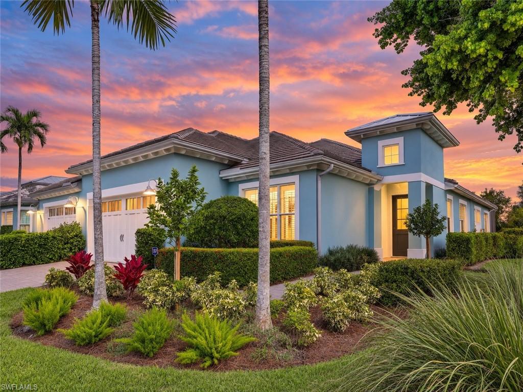 Blue stucco home with a tiled roof, landscaped palms, and glowing windows at sunset.