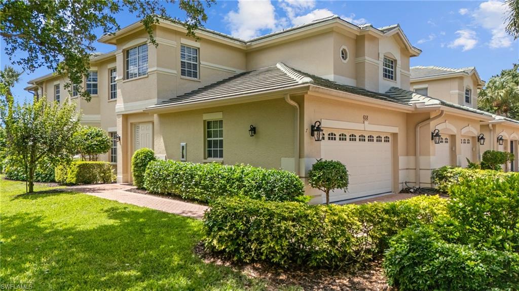 Two-story beige stucco home with a tiled roof, attached garage, and landscaped front lawn.