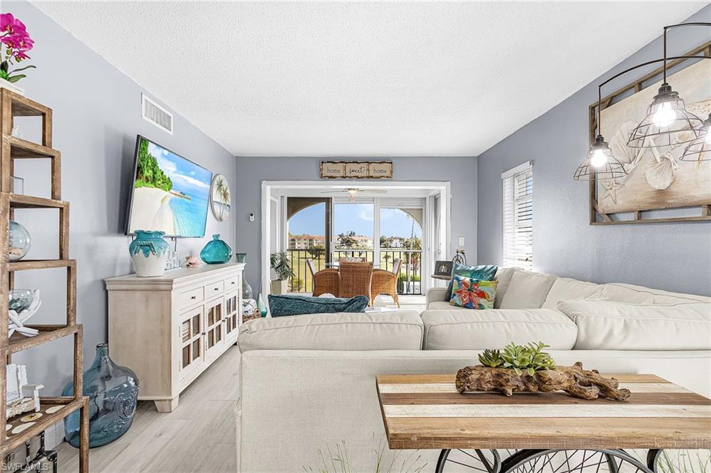 Living room with a white sectional sofa and sliding doors opening to a balcony with wicker seating.