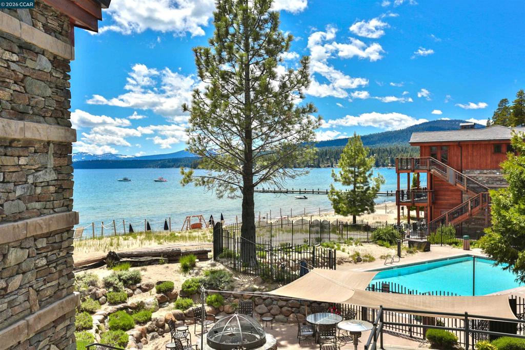Lakeside property with a pool, landscaped patio, sandy shore, and mountain views.