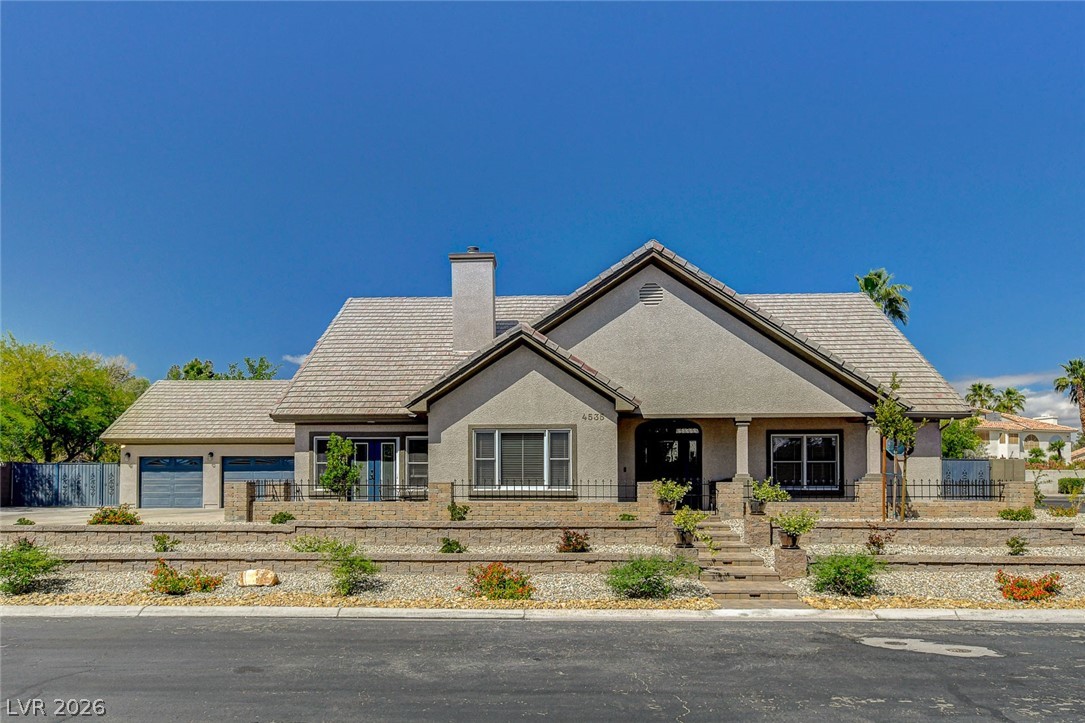 Gray stucco home with gabled roofs, a two-car garage, and tiered desert landscaping.