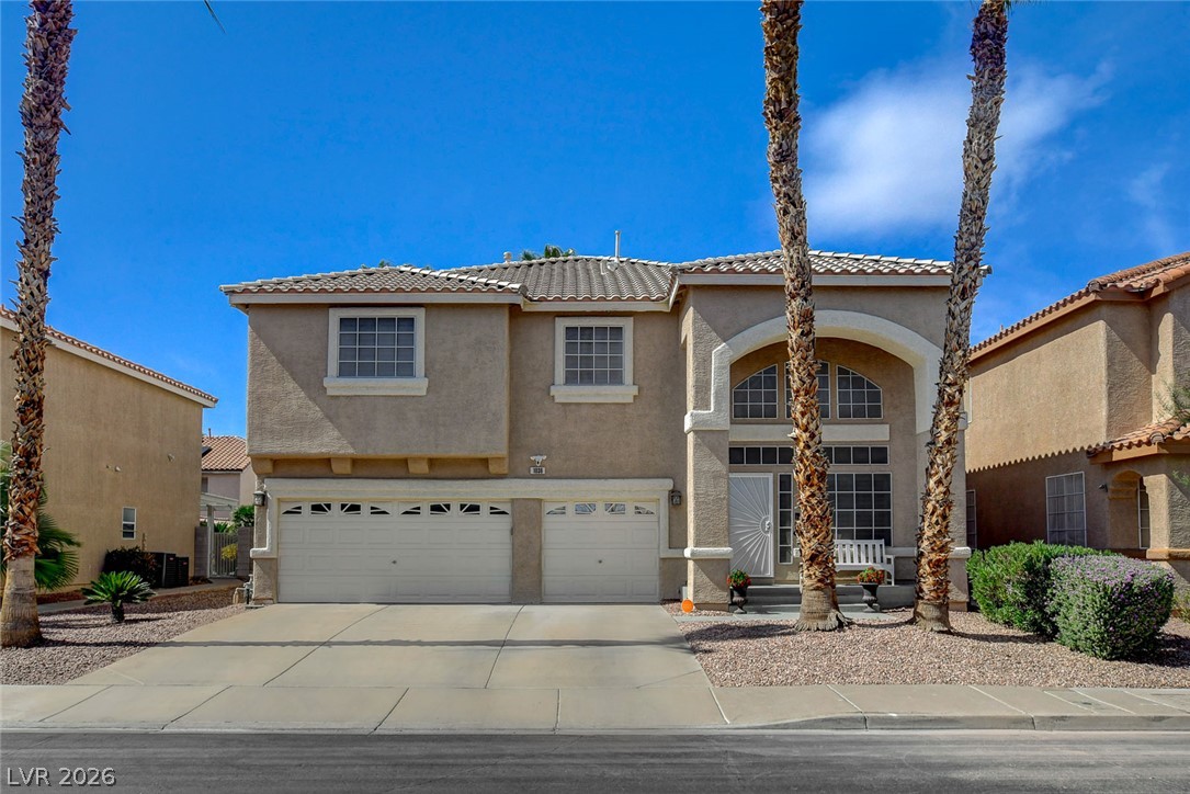 Two-story stucco home with a double garage, arched entry, and palm trees.