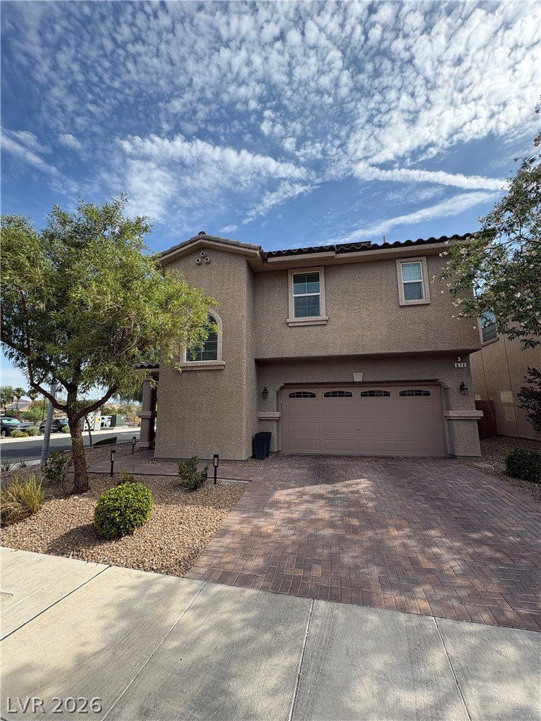 Two-story stucco home with a double garage, paver driveway, and desert landscaping.