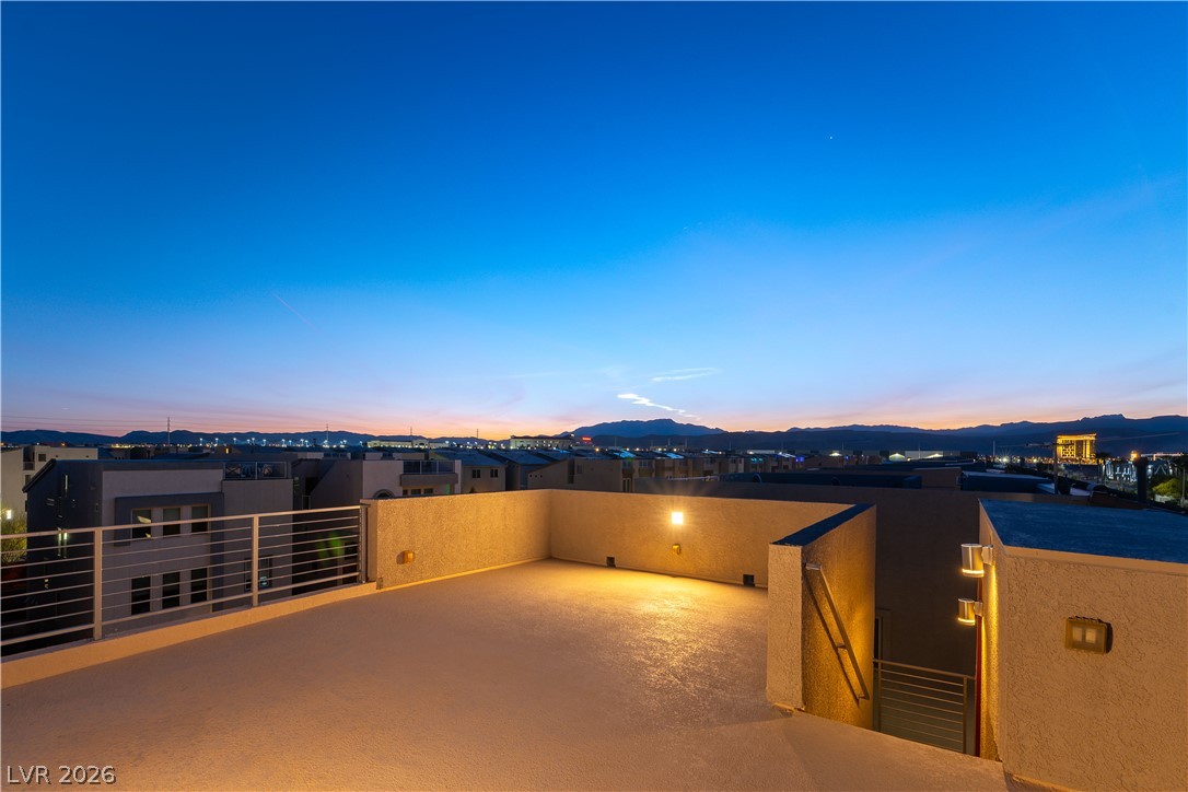 Rooftop terrace overlooking Las Vegas homes and distant mountains at dusk, with warm wall lighting.