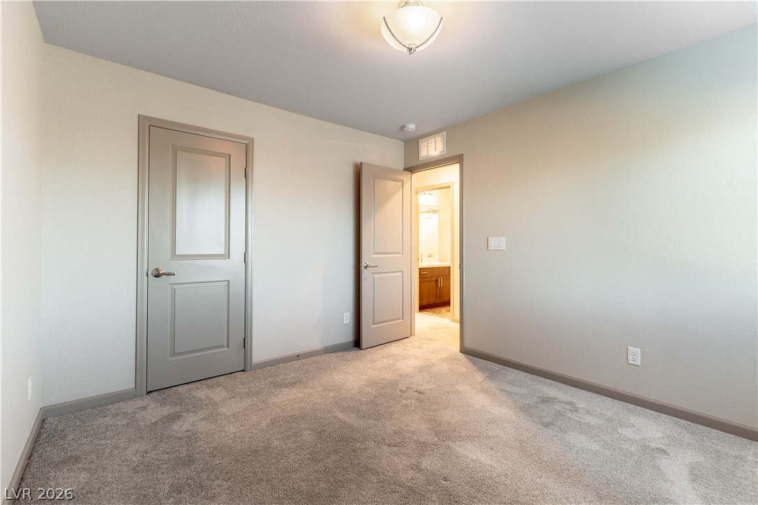 Empty carpeted bedroom with an open doorway revealing a bathroom vanity.
