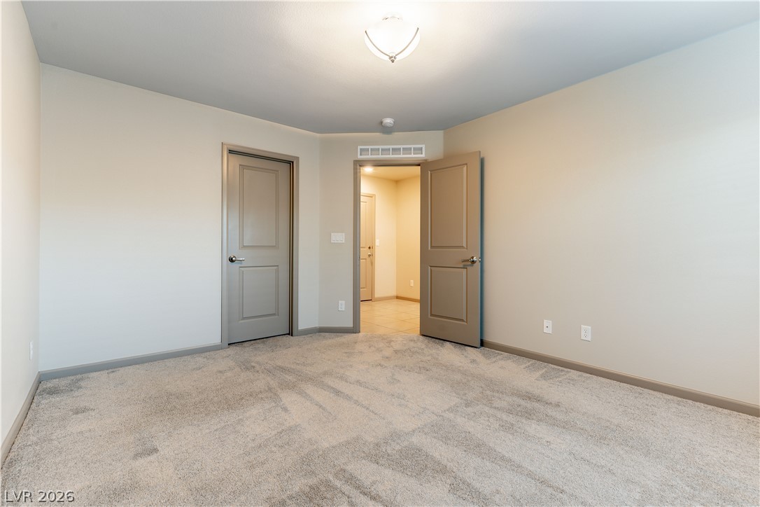 Empty carpeted room with beige walls and an open door to a tiled hallway.