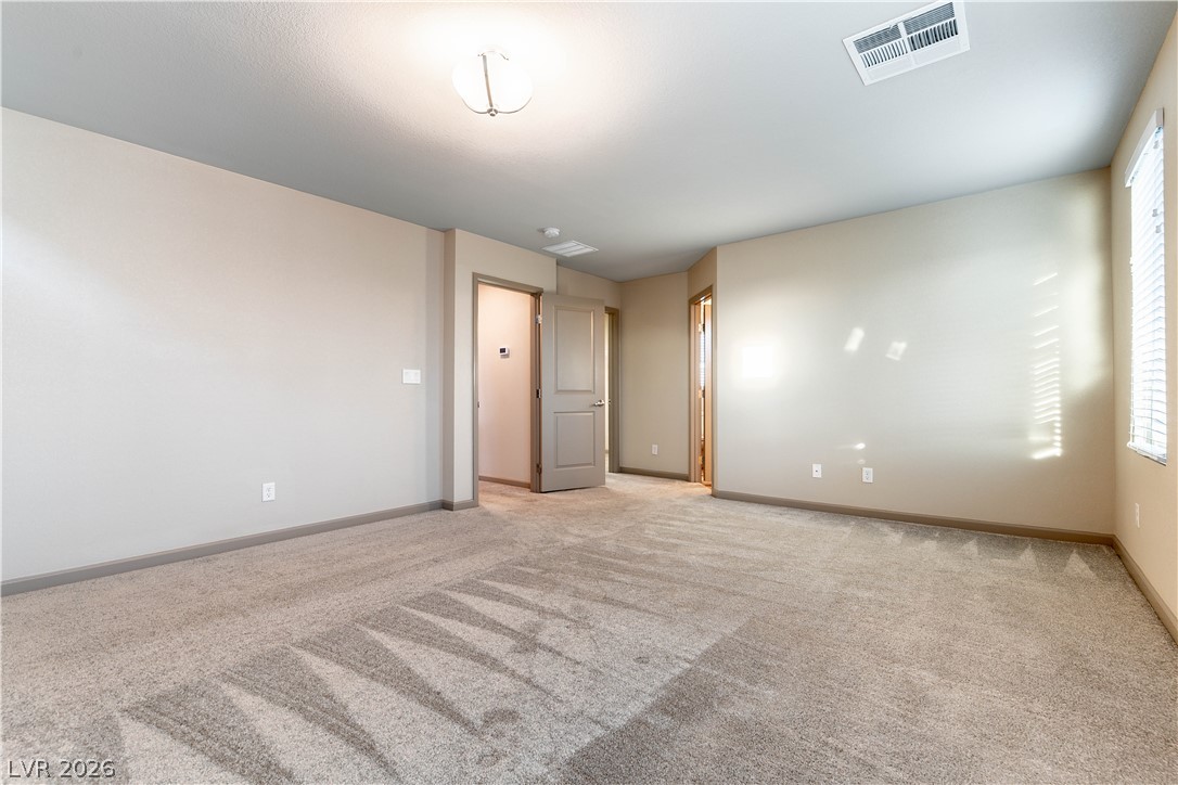 Empty carpeted bedroom with a window and open doorway.