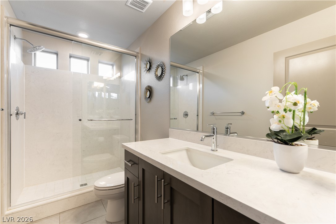 Modern bathroom with a glass-enclosed shower, dark wood vanity, and white orchid on the counter.