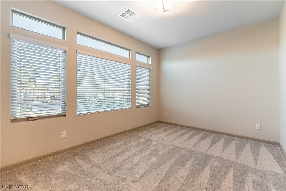 Empty bedroom with beige carpet and three large windows topped by clerestory windows.