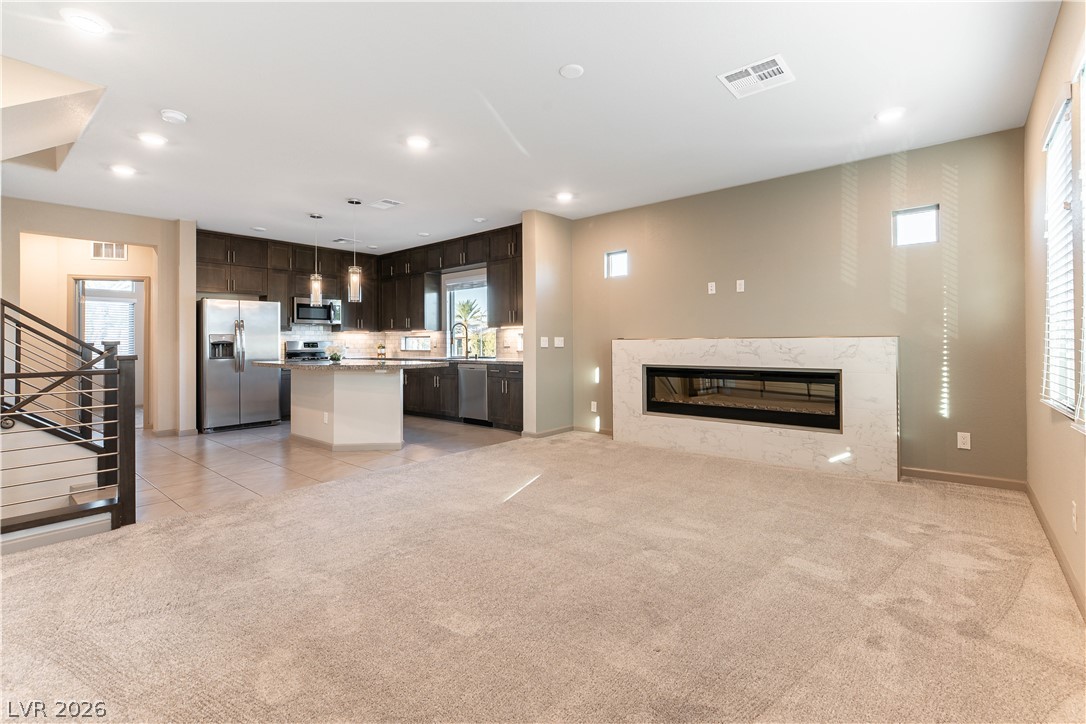 Vacant living room with a marble-surround fireplace opening to a dark-cabinet kitchen.