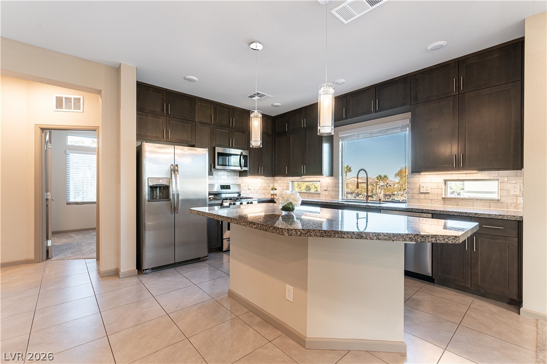 Kitchen with a large granite island, dark cabinets, stainless steel appliances, and a window above the sink.