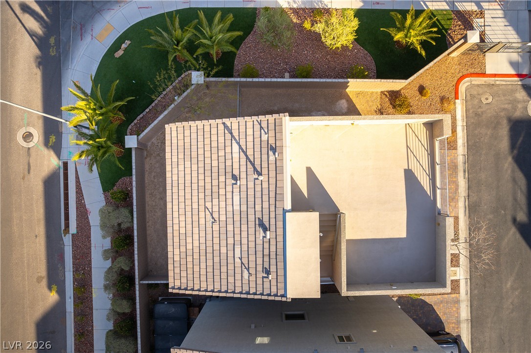 Aerial view of a home with a tiled roof, enclosed flat-roof section, and landscaped yard with palm trees.