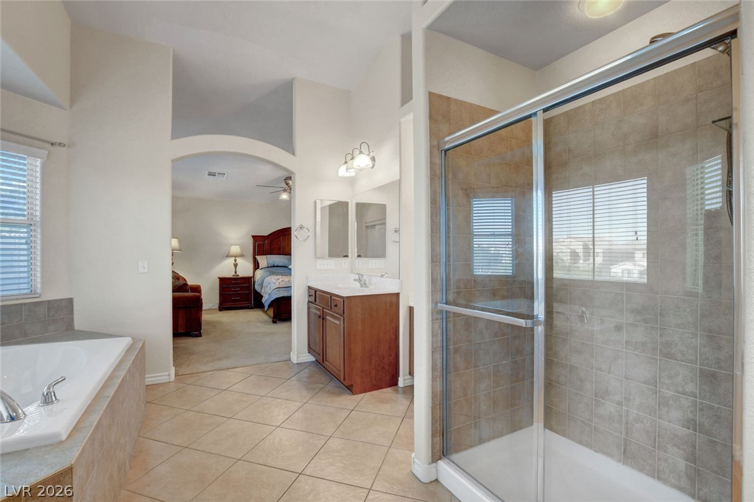 Primary bathroom with a glass-enclosed tiled shower, soaking tub, and arched opening to a bedroom.