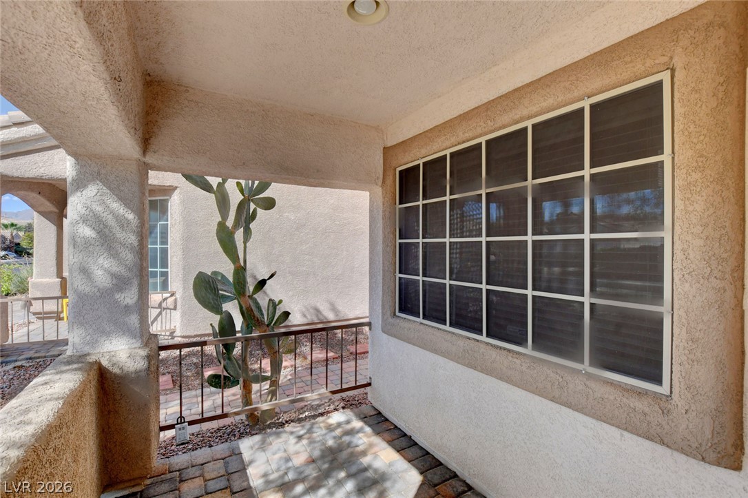Covered stucco patio with a large gridded window, paved floor, and cactus.