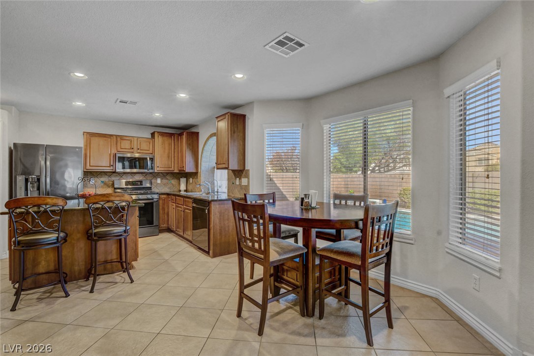 Open kitchen and dining area with wood cabinetry, stainless appliances, and a round table by large windows.