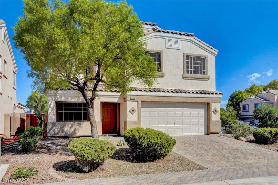 Two-story stucco house with a red front door, attached garage, and desert landscaping.