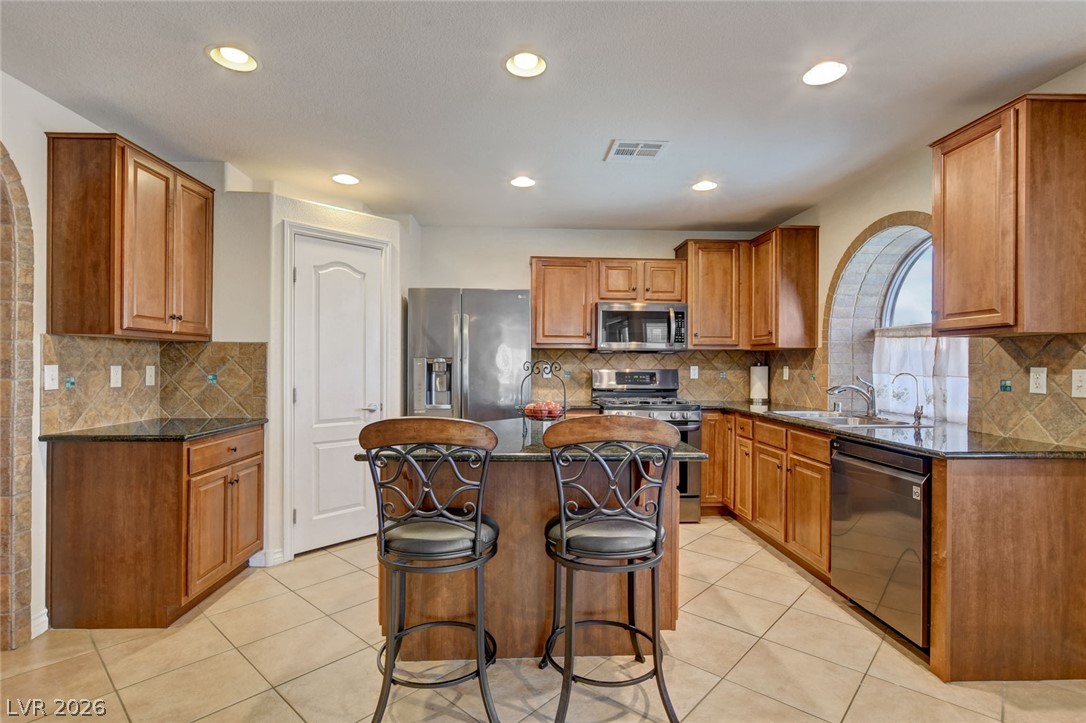 Kitchen with warm wood cabinets, stainless steel appliances, and a central island with two bar stools.