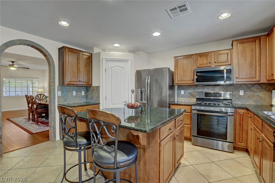 Kitchen with a granite island, bar stools, wood cabinets, and stainless steel appliances.