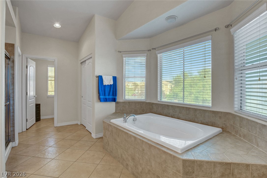 Primary bathroom with a large corner soaking tub beneath windows with white blinds.