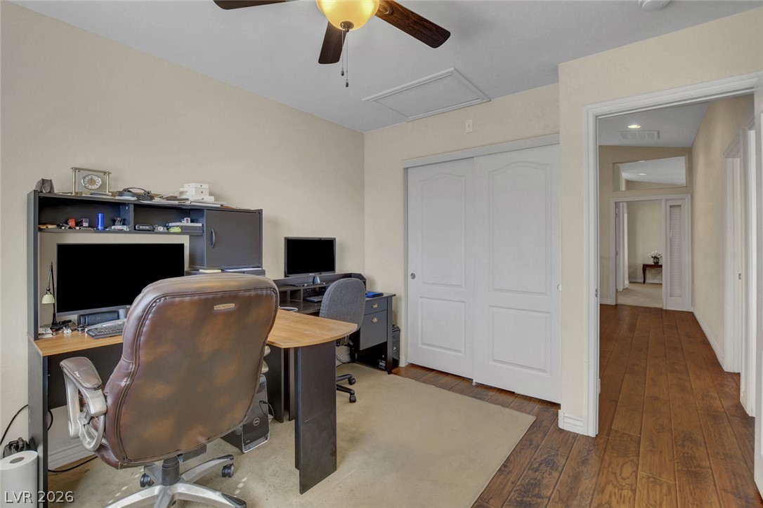 Furnished home office with computer workstations, white closet doors, and a wood-floored hallway.