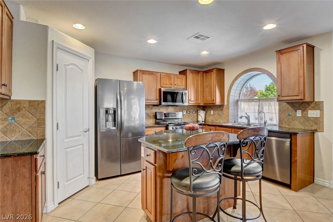 Kitchen with a granite island, stainless steel appliances, warm wood cabinets, and an arched window over the sink.