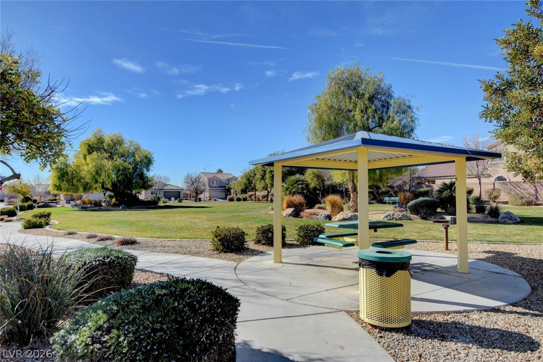 Community park gazebo with green picnic tables beside a paved walkway and landscaped lawn.