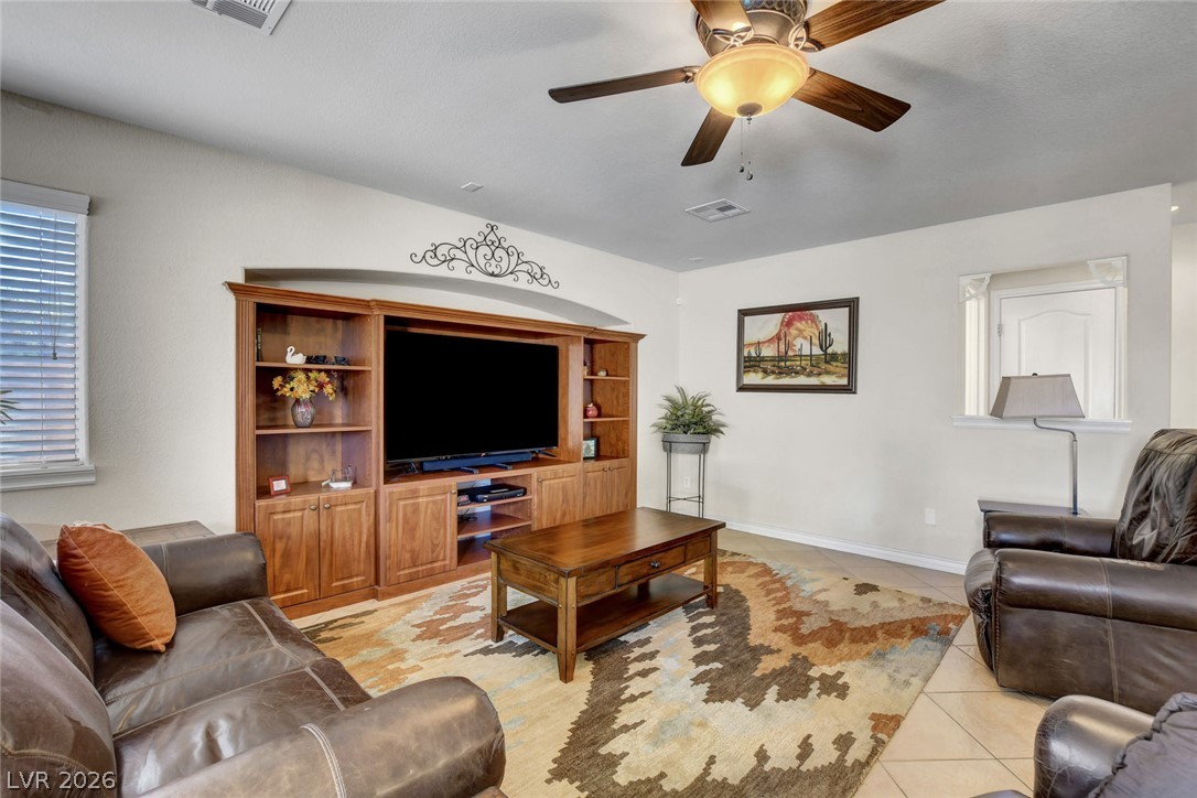 Living room with leather seating, a wood entertainment center, patterned rug, and ceiling fan.
