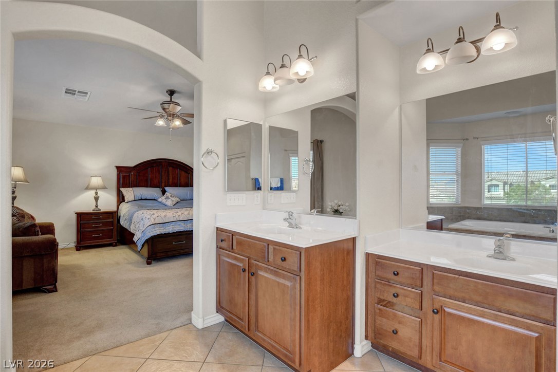Primary bathroom with double wood vanities; adjoining bedroom and window-side bathtub are visible.