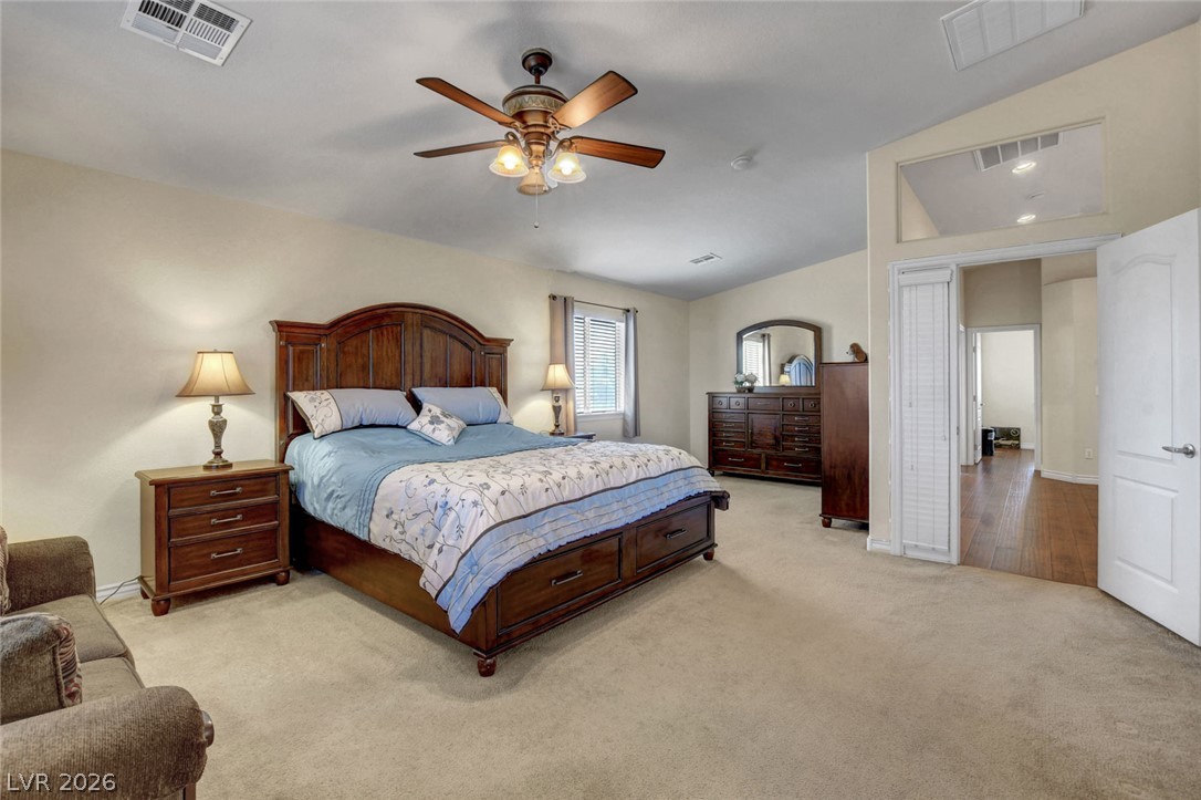 Furnished bedroom with a wooden bed, blue floral bedding, beige carpet, and a ceiling fan.