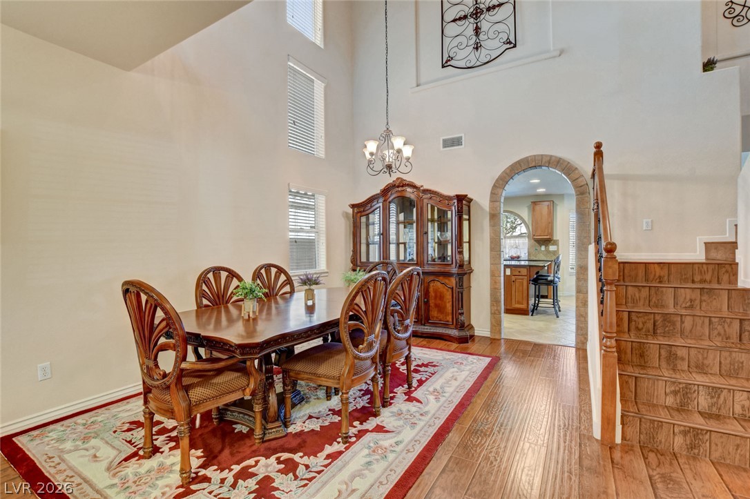 Dining room with a carved wooden table, vaulted ceiling, hardwood floors, and staircase.