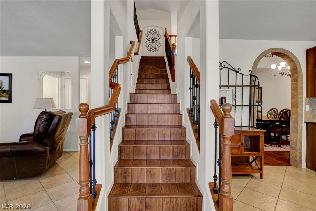 Wood staircase in a tiled foyer, with black metal balusters and a stone-trimmed archway to the dining room.
