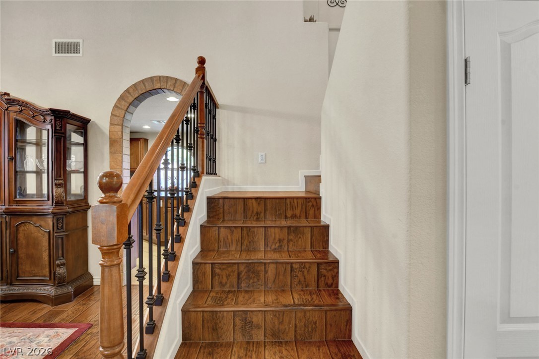 Tiled staircase with a wooden handrail, black balusters, and stone-trimmed archway.