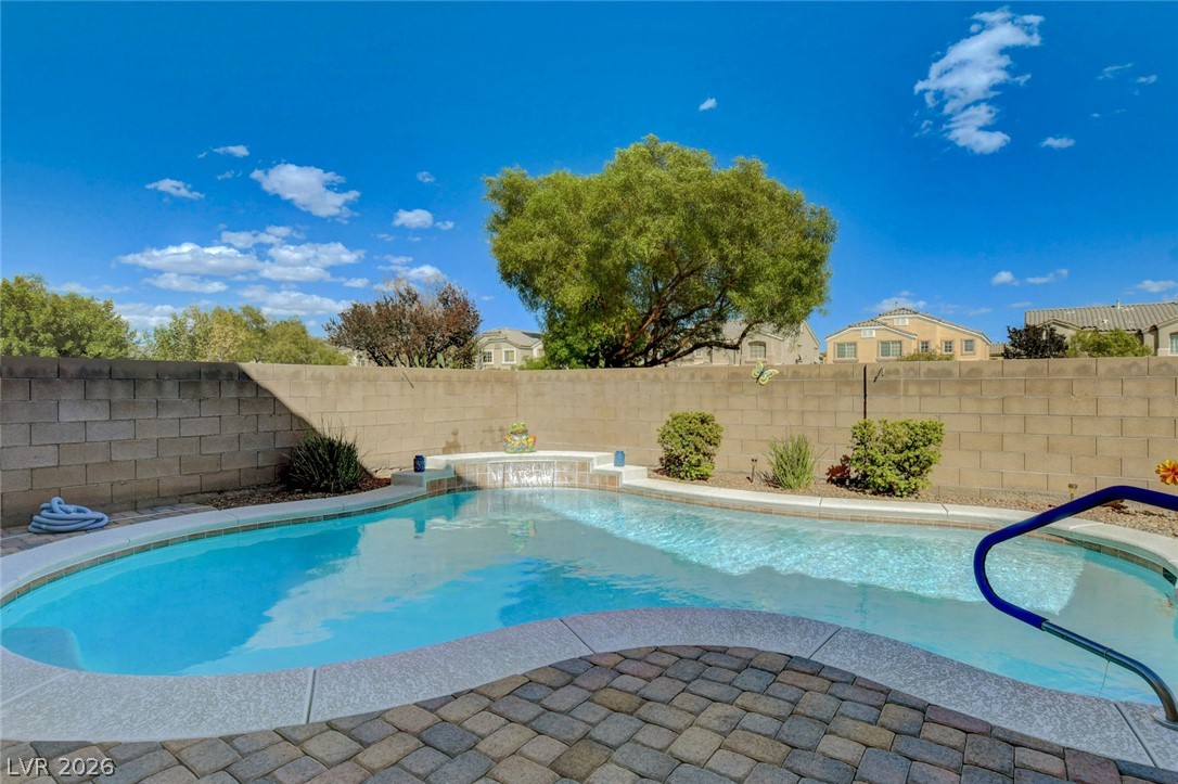 Backyard pool with a raised waterfall and curved handrail beside a paver patio.