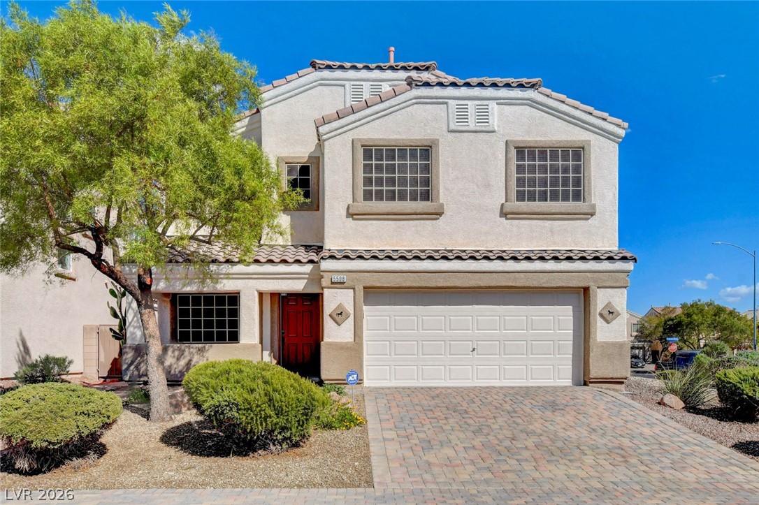Two-story stucco home with a red entry door, white double garage, and desert landscaping.