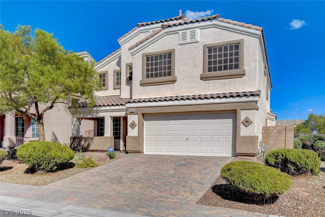 Two-story stucco house with a tile roof, double garage, and paver driveway.