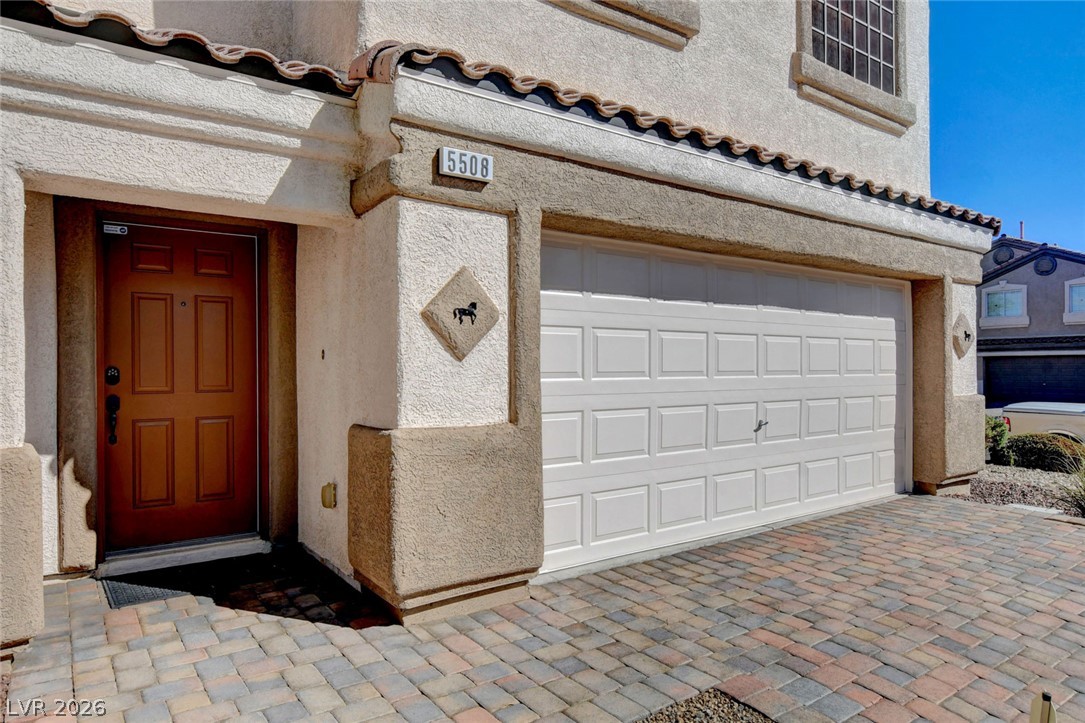 Stucco home exterior with a red entry door, white double garage, and paver driveway.