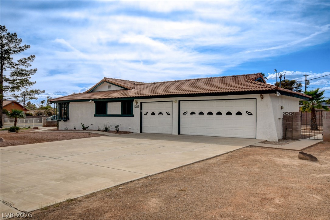 Single-story stucco home with a tile roof, two garage doors, and a wide concrete driveway.