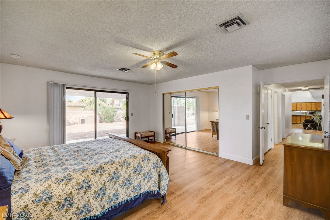 Bedroom with a floral bedspread, wood-look floors, and sliding glass doors to the backyard.