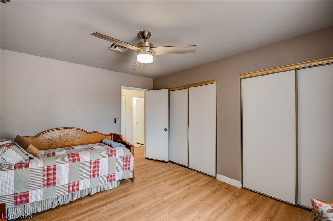 Bedroom with a patchwork-covered daybed, sliding closet doors, wood-look floors, and a ceiling fan.