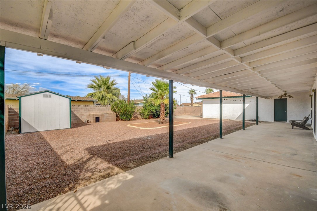 Covered backyard patio overlooking gravel landscaping, a storage shed, and palm trees.
